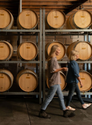 Mother-daughter winemakers Kate & Penelope Radburnd walking past French oak barrels in Radburnd Cellars cellar, Hawke's Bay.